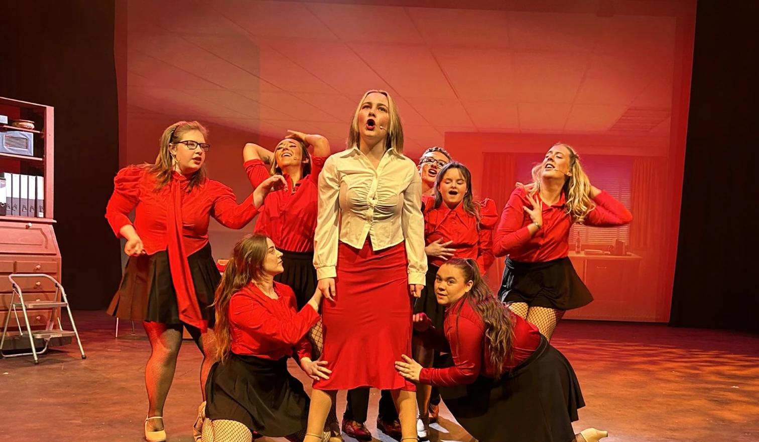 Energetic musical number featuring a group of performers dressed in red, singing passionately on stage. Energetic musical number featuring a group of performers dressed in red, singing passionately on stage.